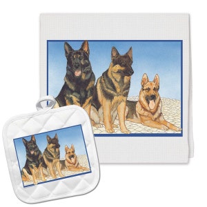 May include: A white kitchen towel with a blue border features a painting of three German Shepherd dogs. The dogs are sitting and lying down on a white background with blue and white cobblestones. The towel is paired with a white quilted pot holder with the same image.