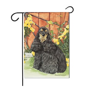 May include: A black and tan American Cocker Spaniel dog sitting in a garden setting with yellow flowers. The dog is looking directly at the viewer.
