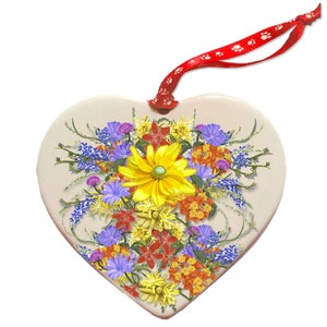 Op de afbeelding: Een hartvormige keramische ornament met een kleurrijk boeket wilde bloemen, waaronder gele, rode, oranje, paarse en blauwe bloemen.