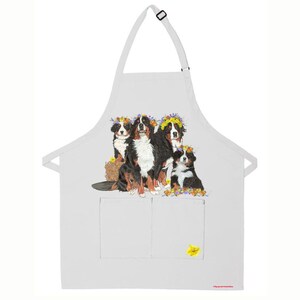 May include: White kitchen apron with a pocket featuring a colorful illustration of four Bernese Mountain Dogs wearing flower crowns.