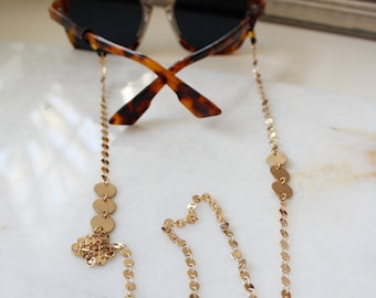 May include: Gold chain with round gold beads, designed to hold sunglasses. The chain is attached to the sunglasses with small loops.