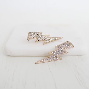 May include: A pair of gold lightning bolt earrings with clear rhinestones.