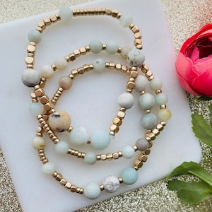 May include: Three layered bracelets with gold beads and light green and white stones.