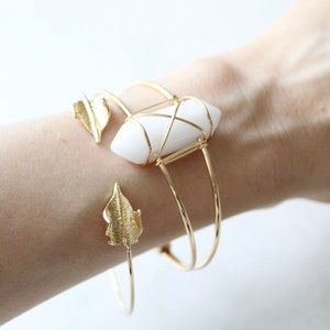 May include: Gold wire wrapped bracelet with a white crystal and leaf accents.