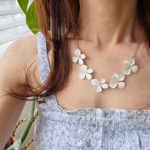 May include: A white flower necklace with gold accents. The necklace is made of ceramic flowers and is strung on a gold chain.