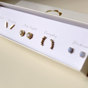 May include: A set of five pairs of gold earrings in a white box. The earrings are labeled "Everyday", "Weekend", "Date Night", "Going Out", and "Everyday".