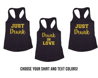 May include: Three black tank tops with gold glitter text. The text on the first tank top reads "Just Drunk". The text on the second tank top reads "Drunk in Love". The text on the third tank top reads "Just Drunk".