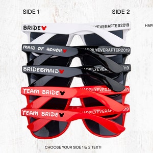 May include: A stack of five pairs of sunglasses with different colored frames and text on the lenses. The top pair is white with the text "BRIDE" and a red Mickey Mouse head. The second pair is white with the text "MAID OF HONOR" and a red Mickey Mouse head. The third pair is black with the text "BRIDESMAID" and a red Mickey Mouse head. The fourth and fifth pairs are red with the text "TEAM BRIDE" and a red Mickey Mouse head.