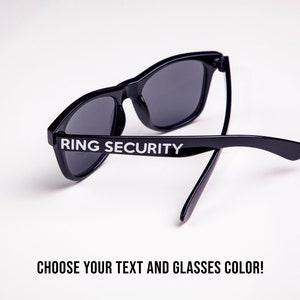 May include: Black sunglasses with the text "RING SECURITY" printed on the frame. Choose your text and glasses color!