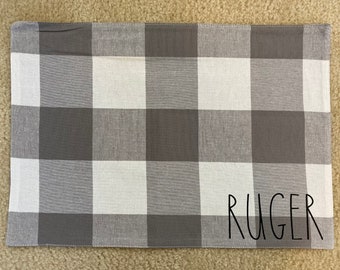 Può includere: Tovaglietta da tavola in tessuto a quadri grigi e bianchi con il nome "RUGER" scritto in corsivo nero.