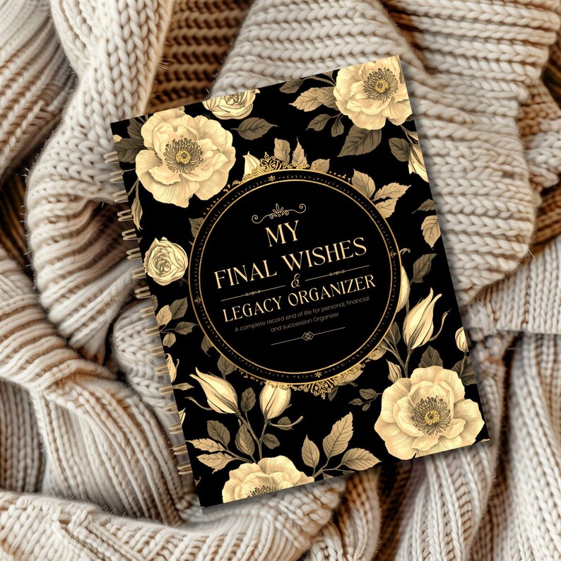 May include: A spiral-bound planner with a black cover featuring cream-colored floral designs and the text "MY FINAL WISHES & LEGACY ORGANIZER." The planner is resting on a beige knitted blanket.