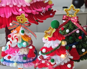 May include: Three decorative tabletop Christmas trees crafted from colorful pipe cleaners. The trees feature layered textures, small pom-poms, gold tinsel stars, and red ribbons. One tree is multi-colored, one is red and white, and one is dark green.