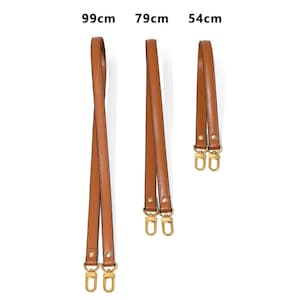 May include: Three brown leather bag straps in varying lengths: 99cm, 79cm, and 54cm. Each strap features gold-colored metal hardware at both ends for attachment. The straps are displayed against a white background.