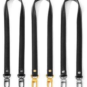 May include: Three black leather purse straps with metal swivel clasps. Two straps have gold-colored clasps, and the other has silver-colored clasps. The straps are shown against a white background.