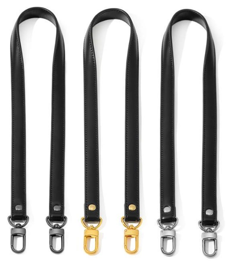 May include: Three black leather purse straps with metal swivel clasps. Two straps have gold-colored clasps, and the other has silver-colored clasps. The straps are shown against a white background.