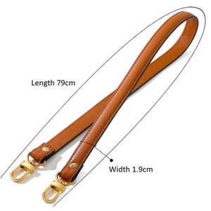 May include: A brown leather handbag strap with gold-colored metal clasps. The strap is 79cm long and 1.9cm wide. The strap is made of a smooth, durable material and is designed to be attached to a handbag or purse.