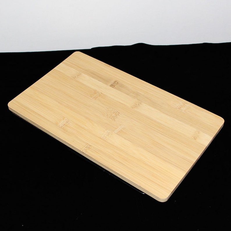 May include: A rectangular bamboo chopping board in a light brown hue. The board is constructed from multiple bamboo strips. The surface is smooth, and the edges are rounded, typical of kitchenware.
