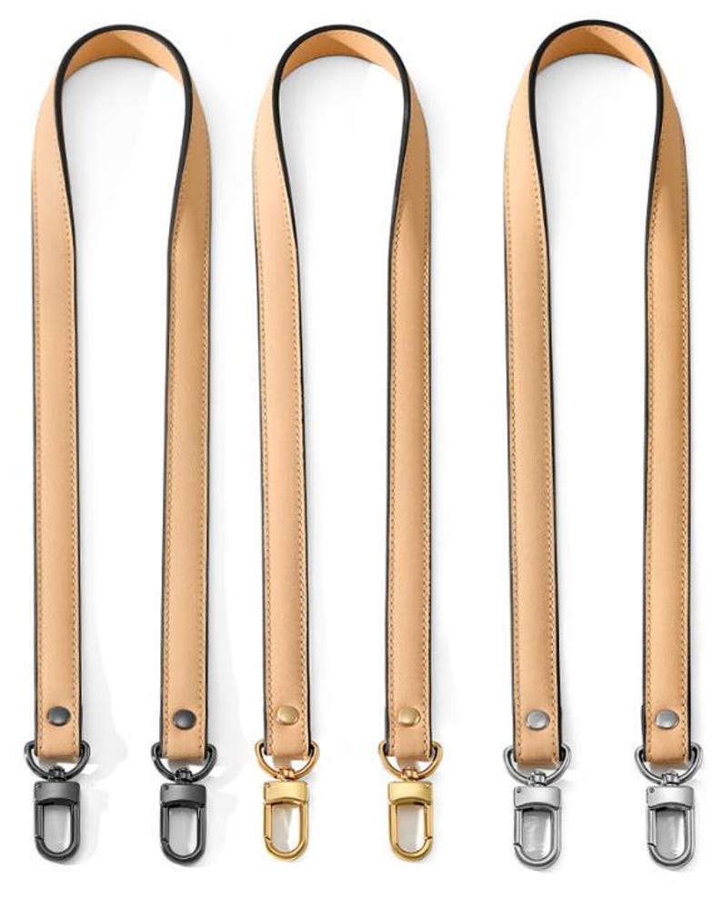 May include: Four beige leather bag straps with black edging and metal hardware. Two straps have silver-tone clasps, and two have gold-tone clasps. The straps are vertically aligned against a white background.