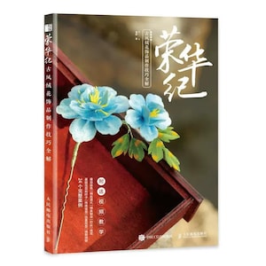 May include: A book cover with the title "荣华纪" in Chinese characters. The cover features a blue and green flower made of fabric, with the text "古风线花饰品制作技巧全解" in Chinese characters. The book is about making fabric flowers.