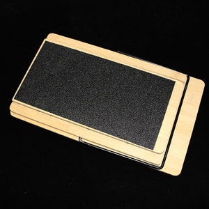 May include: A wooden pet ramp with a black, textured surface. The ramp is made of light-coloured wood and has a foldable design. The ramp is designed to help pets access elevated surfaces.