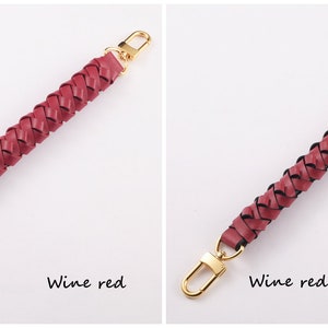 May include: Two braided leather handbag straps with gold metal clasps. The strap on the left is wine red. The strap on the right is wine red with a black trim.