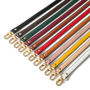 May include: A collection of colorful purse straps in various shades, including black, brown, green, red, and yellow. Each strap features gold-colored metal clasps and rivets, offering a stylish and functional accessory for handbags.