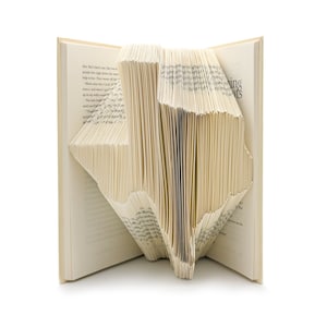May include: A book folded into the shape of the state of Texas. The book is open and the pages are folded to create the outline of the state. The book is on a white background.