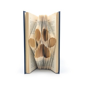May include: A book with pages folded into a 3D flower shape. The book is open and the flower is in the center of the pages. The book is blue on the outside and the pages are cream colored.