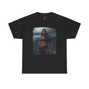 Könnte beinhalten: Schwarzes T-Shirt mit einem quadratischen Bild einer Frau in Kriegerkleidung auf einem Berg. Das Bild zeigt eine Frau in einem schwarzen Crop-Top und Rock, mit einer Bergkette und einem stürmischen Himmel im Hintergrund.