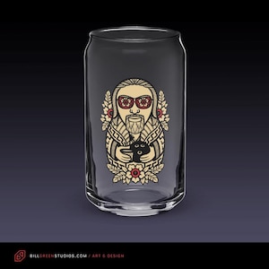 May include: A clear glass can-shaped drinking glass with a detailed illustration. The artwork features a bearded figure wearing sunglasses, holding a black object, surrounded by floral and geometric designs. The glass has a wide mouth and a smooth, cylindrical shape.