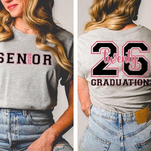 May include: A gray t-shirt with the word "SENIOR" in black and pink lettering on the front, and "26 Twenty GRADUATION" on the back. The shirt is worn with blue jeans.
