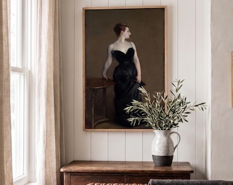 Puede incluir: Un retrato enmarcado de una figura con vestido negro de pie junto a una mesa, expuesto en una pared con paneles blancos sobre una cómoda de madera. Una jarra de cerámica blanca con ramas de olivo se encuentra sobre la cómoda junto al cuadro.
