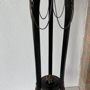 May include: A black wooden plant stand with gold accents and chains. The stand has a round top and three legs.