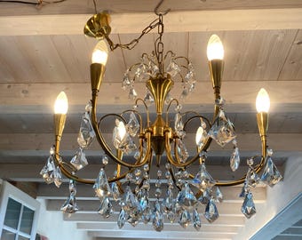 May include: A vintage brass chandelier with six illuminated candle-style bulbs and hanging crystal accents. The fixture is suspended from the ceiling and features curved arms and decorative details, adding a touch of elegance to the room.