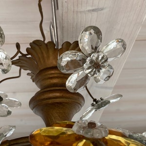 May include: A gold-toned chandelier with crystal flower accents. The chandelier features clear and amber glass flowers.