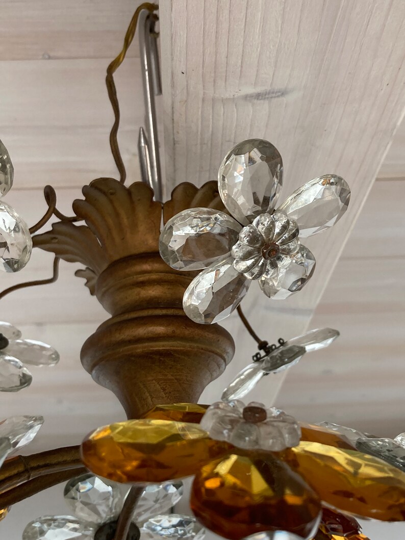 May include: A gold-toned chandelier with crystal flower accents. The chandelier features clear and amber glass flowers.