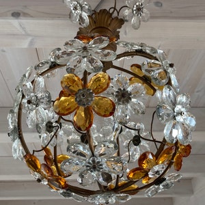 May include: A gold-toned chandelier with a round shape, featuring clear and amber glass flower-shaped crystals. The chandelier is suspended from a chain.
