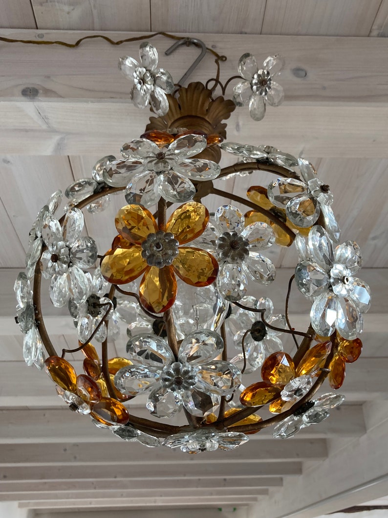 May include: A gold-toned chandelier with a round shape, featuring clear and amber glass flower-shaped crystals. The chandelier is suspended from a chain.