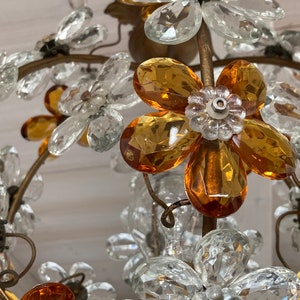May include: A crystal chandelier with amber and clear glass flower accents. The chandelier has a gold metal frame and is designed in a floral motif.
