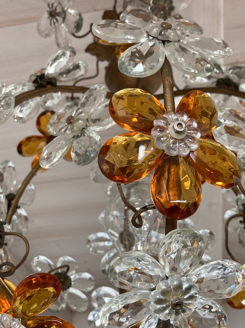 May include: A crystal chandelier with amber and clear glass flower accents. The chandelier has a gold metal frame and is designed in a floral motif.