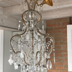 May include: A crystal chandelier with a gold-toned metal frame and many clear crystal drops. The chandelier is hanging from a white ceiling.