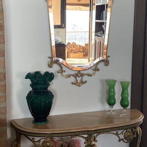 Könnte beinhalten: Ein goldfarbener Konsolentisch mit einer Marmorplatte. Der Tisch hat verzierte Beine und ein dekoratives Design. Eine grüne Glasvase mit Blumenmuster steht auf dem Tisch, zusammen mit zwei grünen Glasvasen. Ein Blumenstrauß in einer klaren Glasvase steht auf dem Tisch.