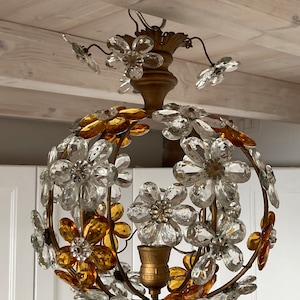 May include: A gold-toned chandelier with a round, spherical shape. The chandelier is adorned with clear and amber glass flowers. The flowers are arranged in a circular pattern around the light fixture.
