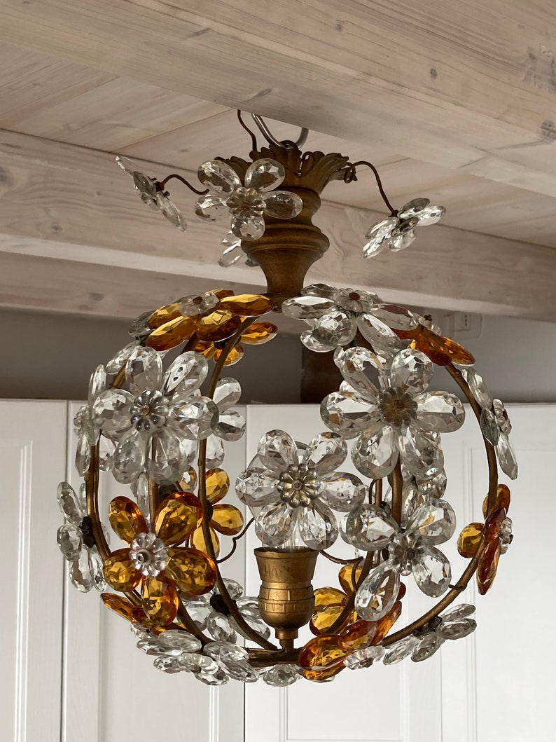 May include: A gold-toned chandelier with a round, spherical shape. The chandelier is adorned with clear and amber glass flowers. The flowers are arranged in a circular pattern around the light fixture.