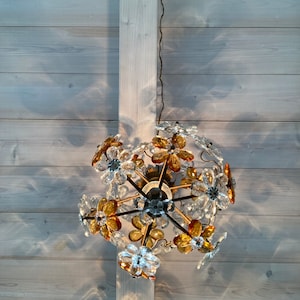 May include: A chandelier with a floral design featuring clear and amber glass flowers. The chandelier is hanging from a white ceiling.