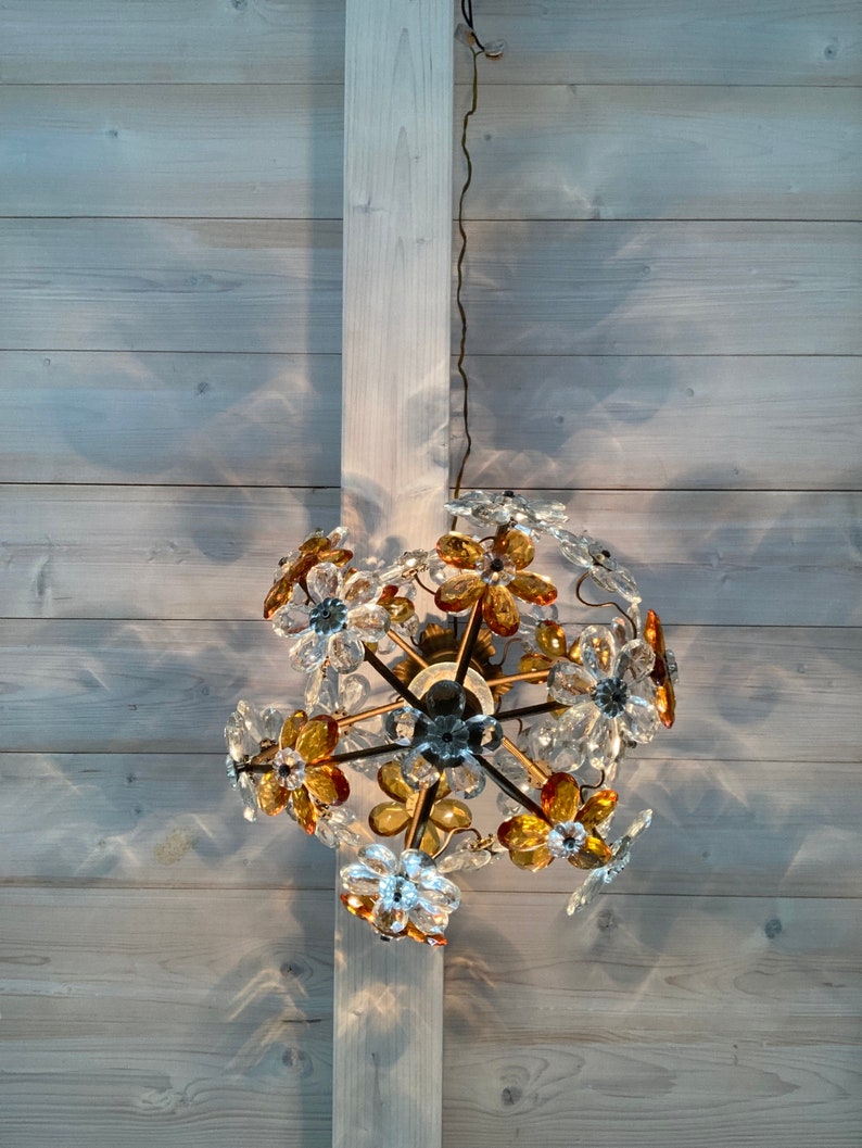 May include: A chandelier with a floral design featuring clear and amber glass flowers. The chandelier is hanging from a white ceiling.