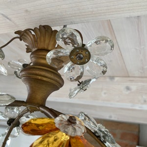 May include: Close-up of a gold-toned chandelier with clear and amber glass crystals shaped like flowers. The chandelier has a floral design with multiple tiers of crystals.