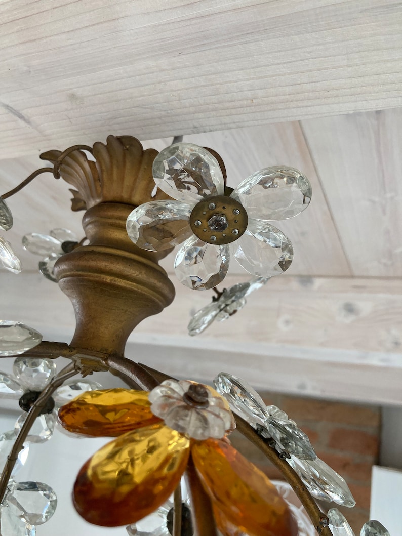 May include: Close-up of a gold-toned chandelier with clear and amber glass crystals shaped like flowers. The chandelier has a floral design with multiple tiers of crystals.