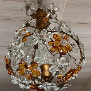 May include: A gold-toned chandelier with a round, wire frame adorned with clear and amber glass flower-shaped crystals.