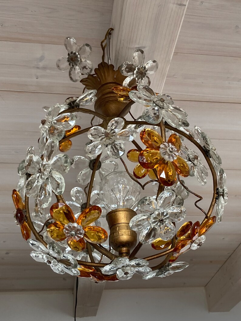 May include: A gold-toned chandelier with a round, wire frame adorned with clear and amber glass flower-shaped crystals.